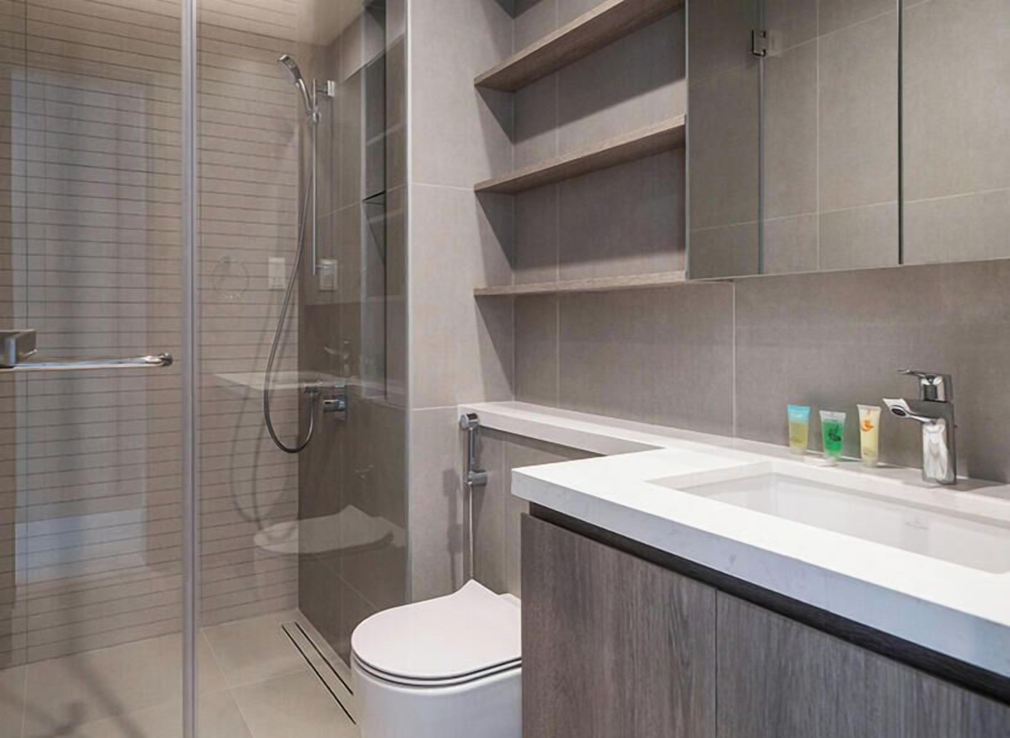 Un baño moderno con ducha envuelta en vidrio, inodoro blanco y tocador con lavamanos y dispensadores de jabón.