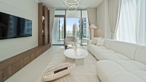 A modern living room with a large flat-screen TV, a white sofa, a round coffee table, and a view of tall buildings through large windows. - Experience 2BR Luxury Living  LIV Marina (Dubai)
