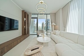 Ein modernes Wohnzimmer mit großem Flachbildfernseher, einem weißen Sofa, einem runden Couchtisch und Blick auf hohe Gebäude durch große Fenster.