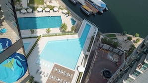 A rooftop pool area with multiple swimming pools, sun loungers, and a dock with boats. - Experience 2BR Luxury Living  LIV Marina (Dubai)