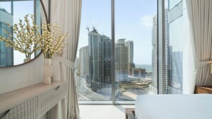 A modern hotel room with a large window offering a city view, a wooden bedside table, and a decorative vase with flowers. - Experience 2BR Luxury Living  LIV Marina (Dubai)