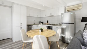 Eine moderne Küche mit weißen Schränken, einem Edelstahlkühlschrank und einem runden Holzes Esstisch mit vier Stühlen.