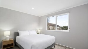 Ein Schlafzimmer mit einem großen Bett, zwei Nachttischen mit Lampen, einem Fenster mit Ausblick und einer grauen Wand.