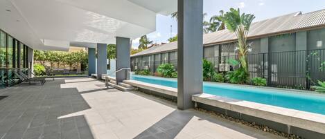An outdoor pool area with a modern design, featuring a pool, seating, and a covered walkway.