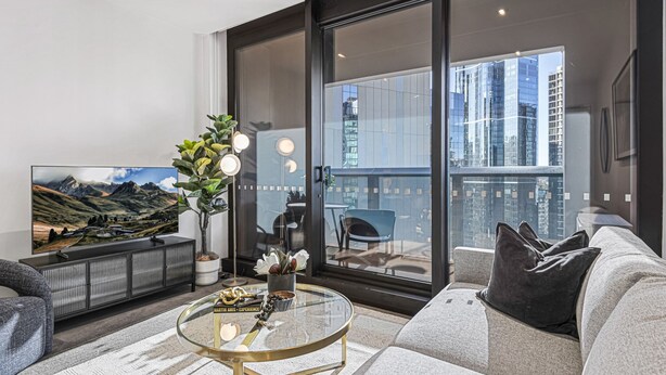 A modern living room with a large flat-screen TV, a glass coffee table, a sofa, and a balcony with a city view. - Elegant Southbank Escape Apartment with Balcony (Southbank)