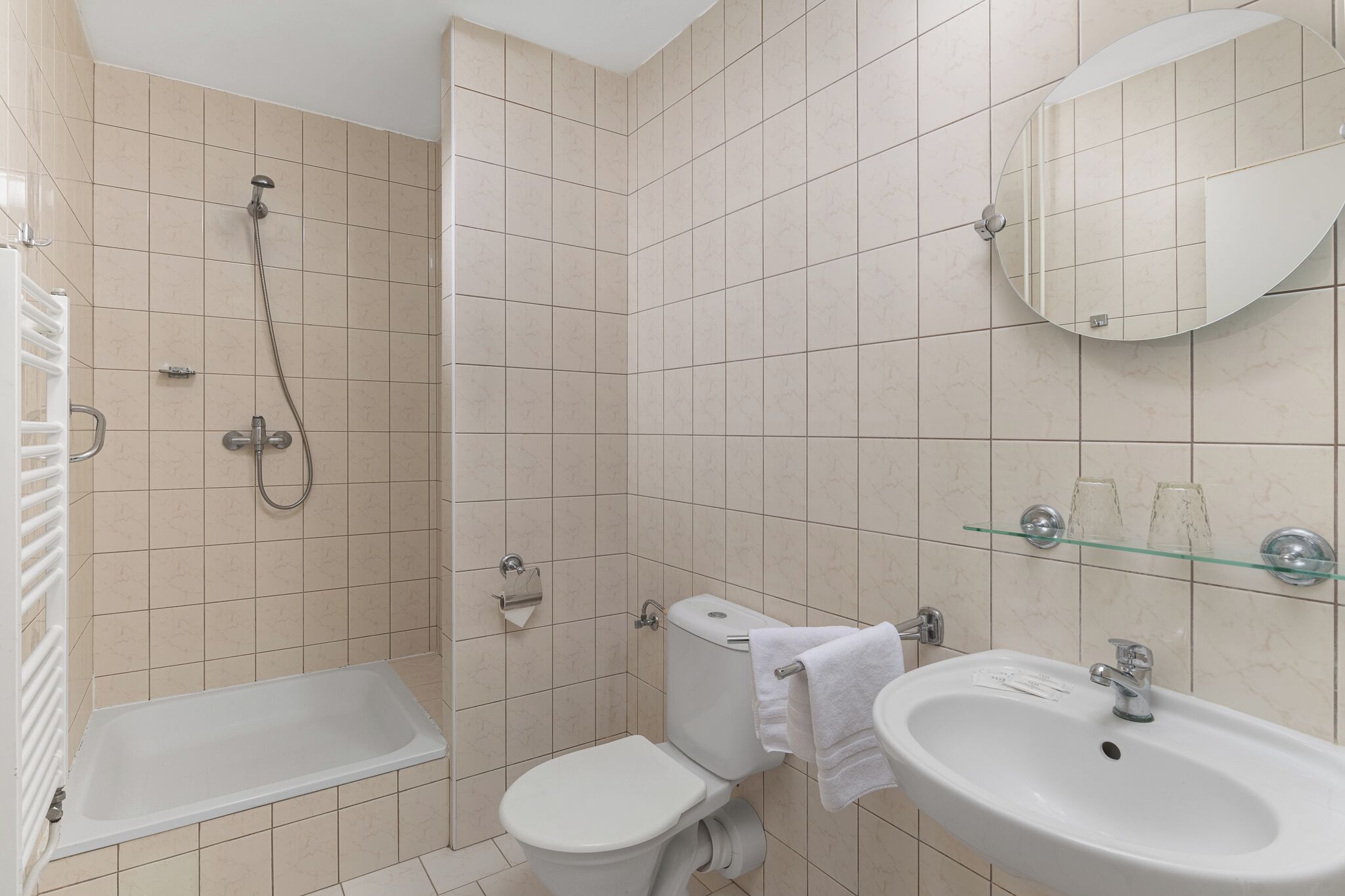 A bathroom with a bathtub, toilet, sink, and a glass shelf with two glasses.