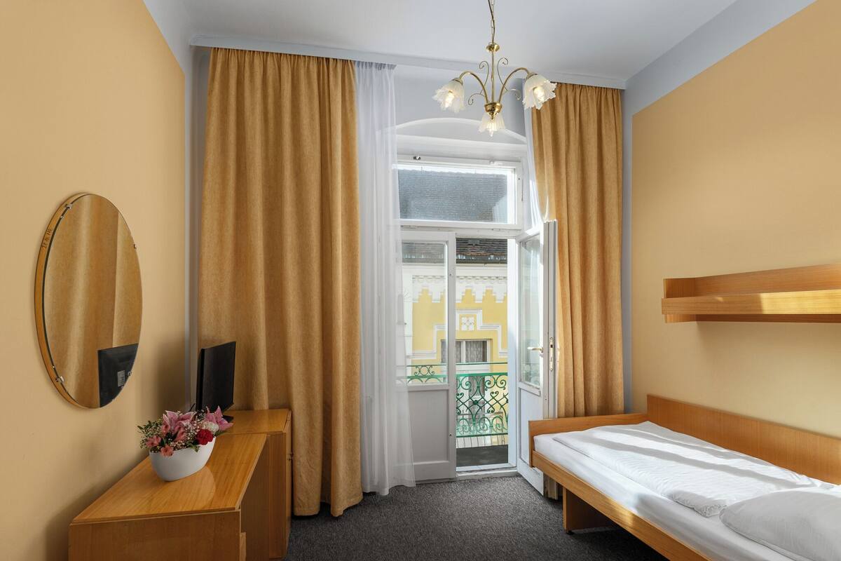 Una habitación de hotel con una cama, un aparador de madera, un espejo y una ventana con cortinas.