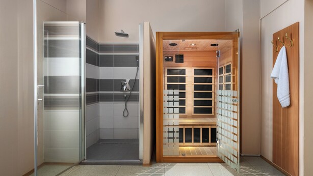 A modern bathroom with a glass shower enclosure, a wooden sauna, and a towel rack. - Hotel Goethe Spa & Medical (Františkovy Lázně)