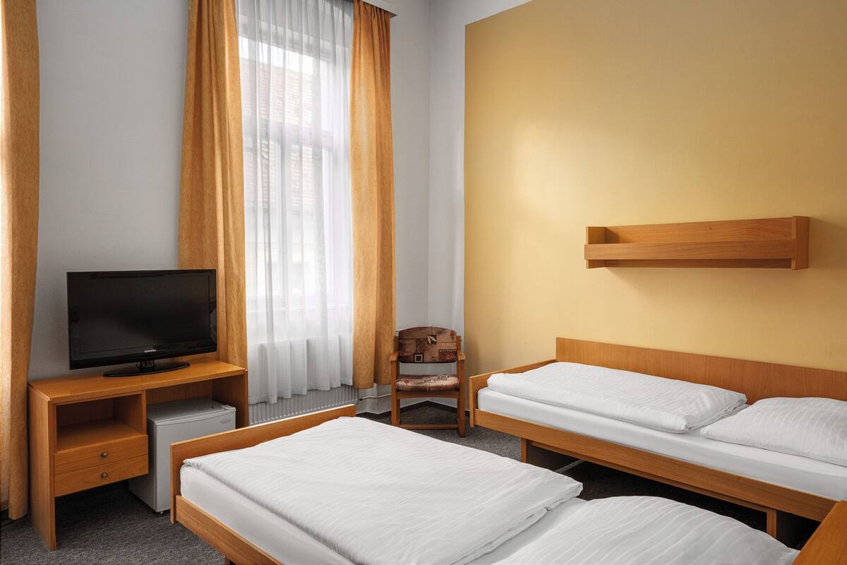 Habitación de hotel con dos camas individuales, un televisor sobre un escritorio de madera, un refrigerador pequeño y una silla.