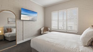 A bedroom with a large bed, a TV mounted on the wall, a window with shutters, and a mirror.