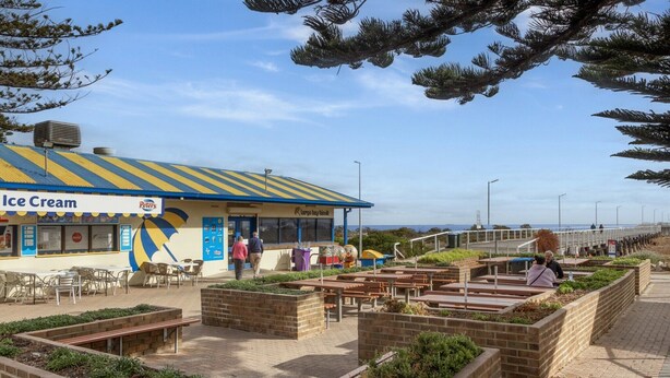An outdoor seating area with tables and benches, a building labeled "Ice Cream," and a view of the beach in the background.