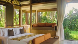 Een slaapkamer met een groot bed, een bank en uitzicht op een weelderige tuin.