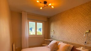 A bedroom with a bed, bedside tables, a window, and a ceiling light fixture. - La parenthèse bleue, loggia and parking lot (Courseulles-sur-Mer)