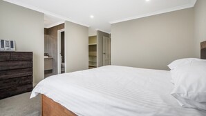 A bedroom with a large bed, a wooden dresser, and a walk-in closet. - Spacious 4-Bed House with Outdoor Area (Byford)