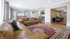 A modern living room with a brown leather sofa, a red patterned rug, and a dining area in the background. - Spacious 4-Bed House with Outdoor Area (Byford)