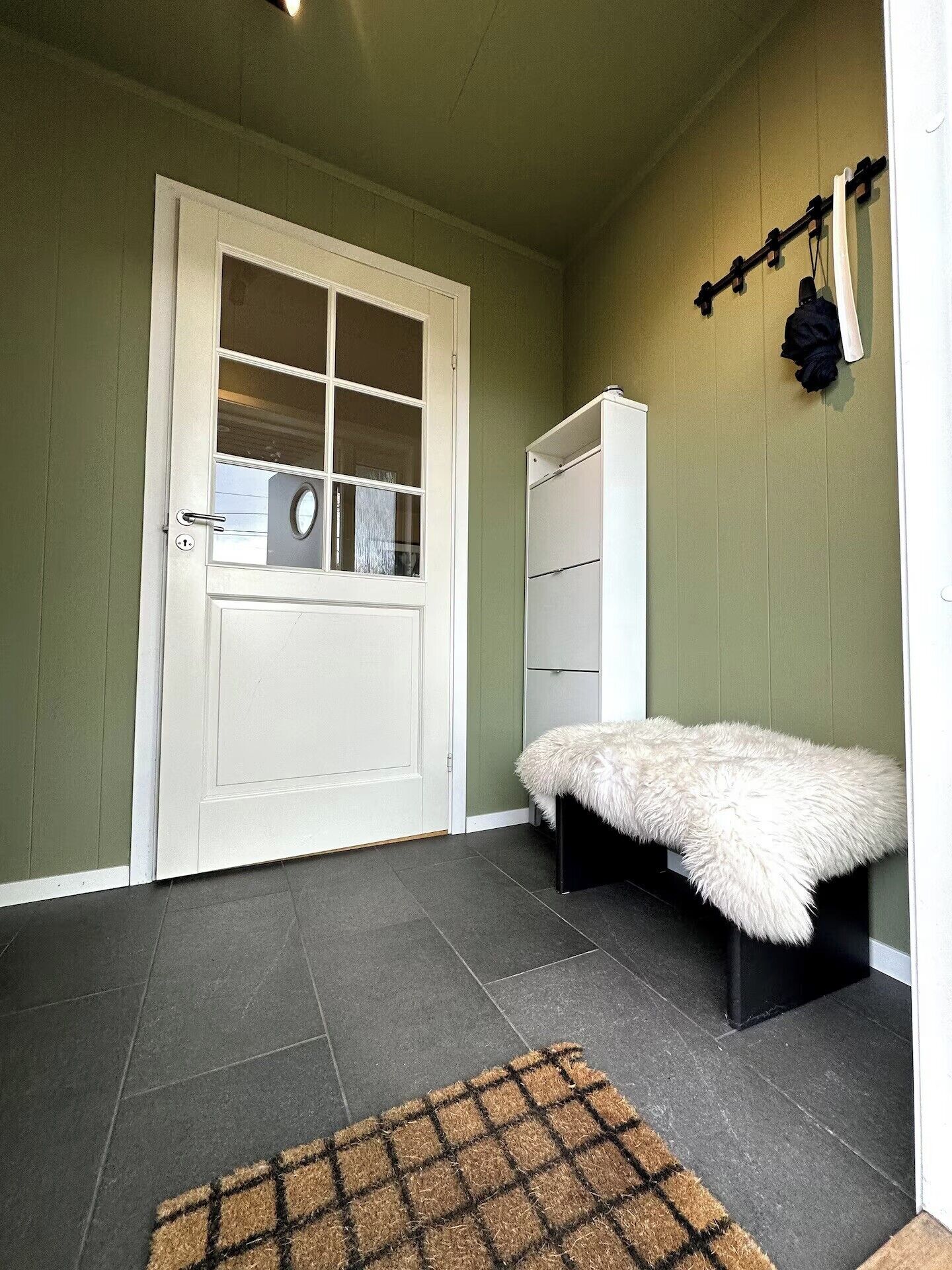 Een kamer met een witte deur, een witte kledingkast, een zachte witte bank en een bruine deurmat.