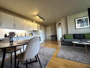 Et moderne køkken med hvide skabe, et spisebord med stole, en grå sofa og et billede i ramme på væggen.