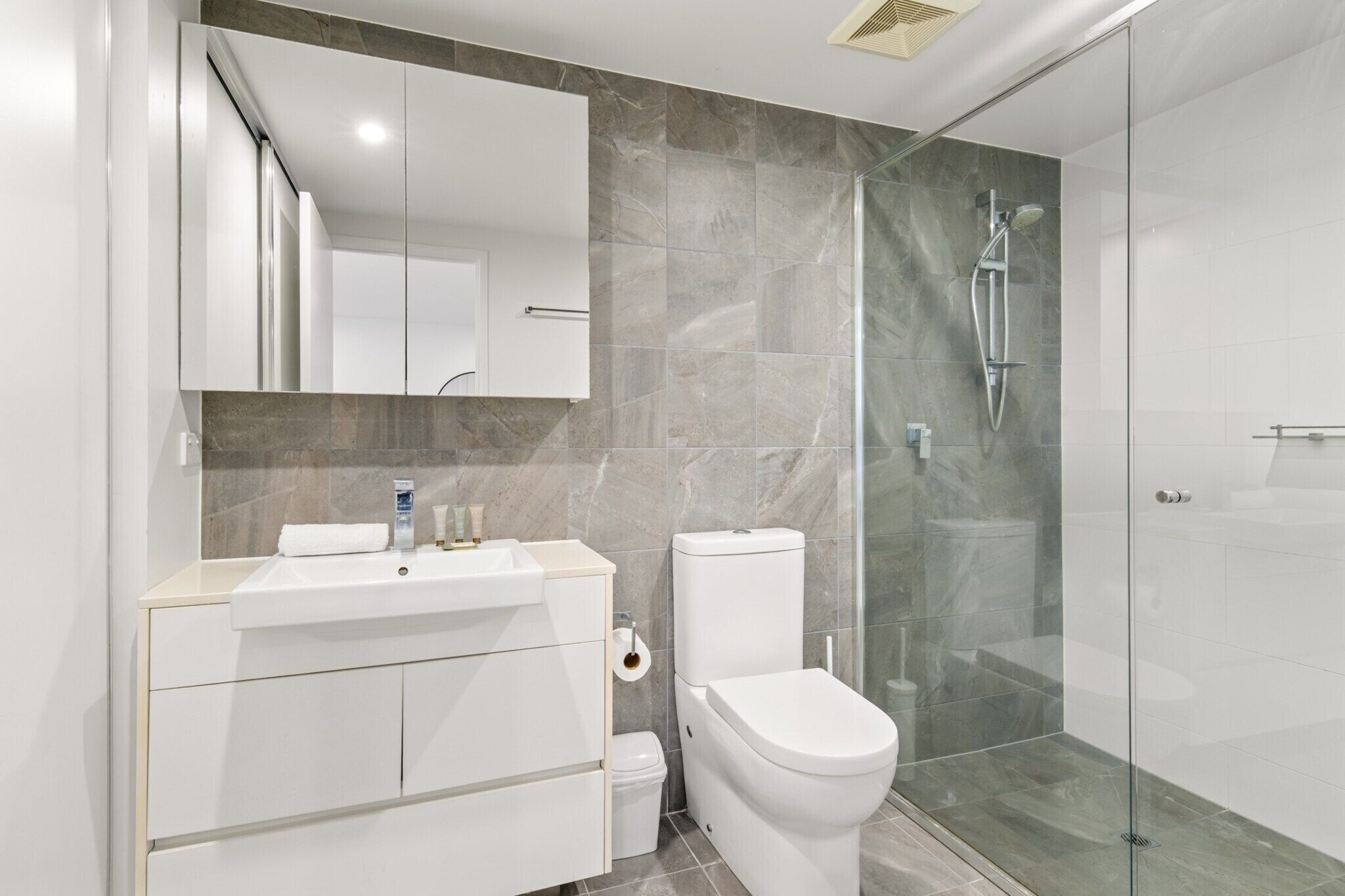 Een moderne badkamer met een douchecabine van glas, een witte wastafel en een toilet.