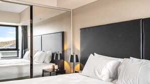 Ein modernes Hotelzimmer mit einem großen Bett, einem Nachttisch mit Lampen und einem großen Spiegel, der den Raum widerspiegelt.