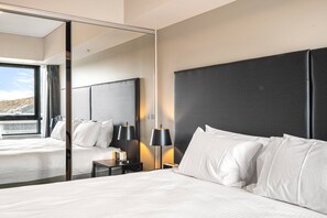 A modern hotel room with a large bed, a nightstand with lamps, and a large mirror reflecting the room. - Spacious Apartment in Heart of Southbank (Southbank)