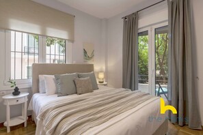 A bedroom with a bed, bedside table, lamp, and a view through a window. - Sun-Splashed Sanctum w/ Green Patio, Acropolis (Athens)