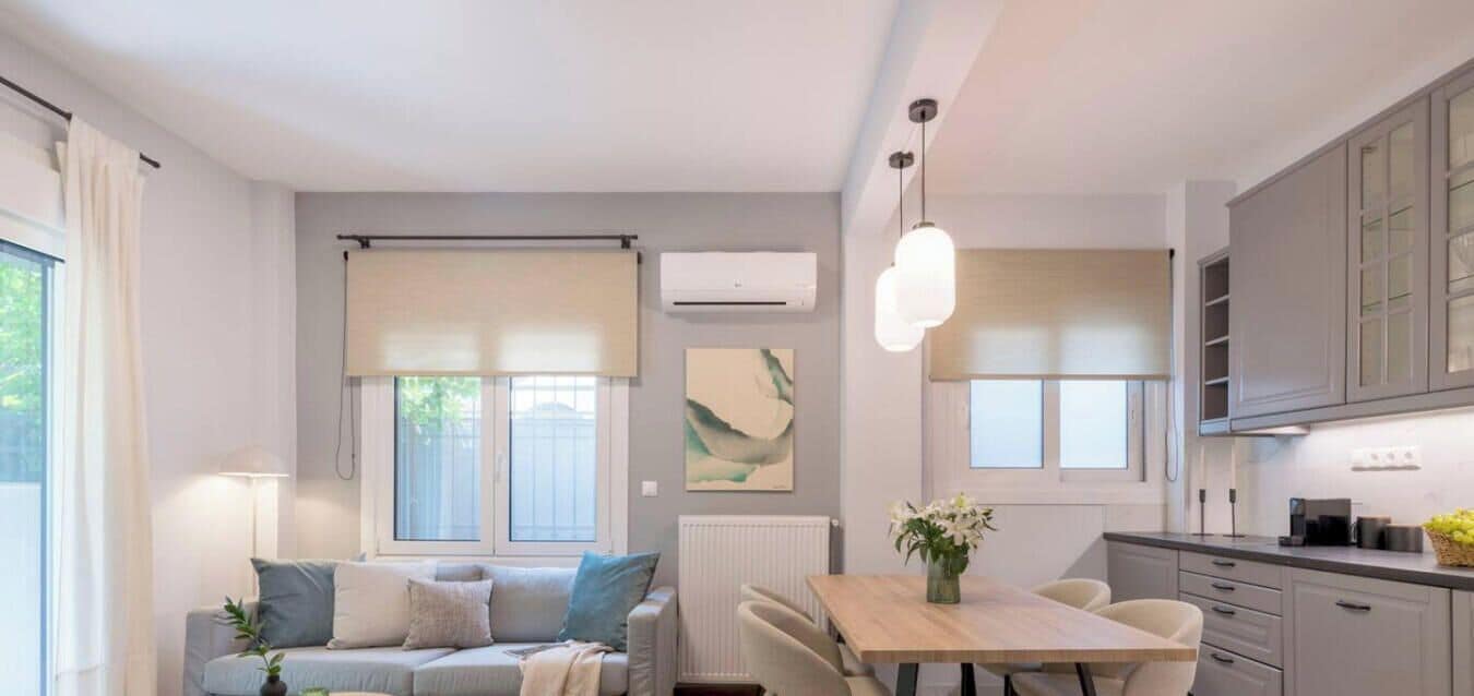 A modern living room with a sofa, a dining table, and a kitchen area with cabinets and a window.