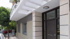 Un edificio con puerta de cristal grande, ventana con barrotes y fachada blanca con líneas horizontales.