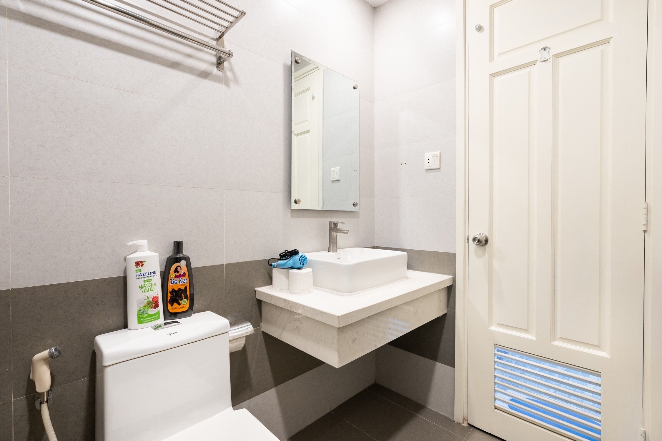 A bathroom with a toilet, sink, mirror, and a door with a vent.