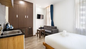 Una habitación de hotel con cama, sofá, una mesita, televisión y kitchenette.