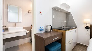 Habitación de hotel pequeña con lavamanos, espejo y una kitchenette.