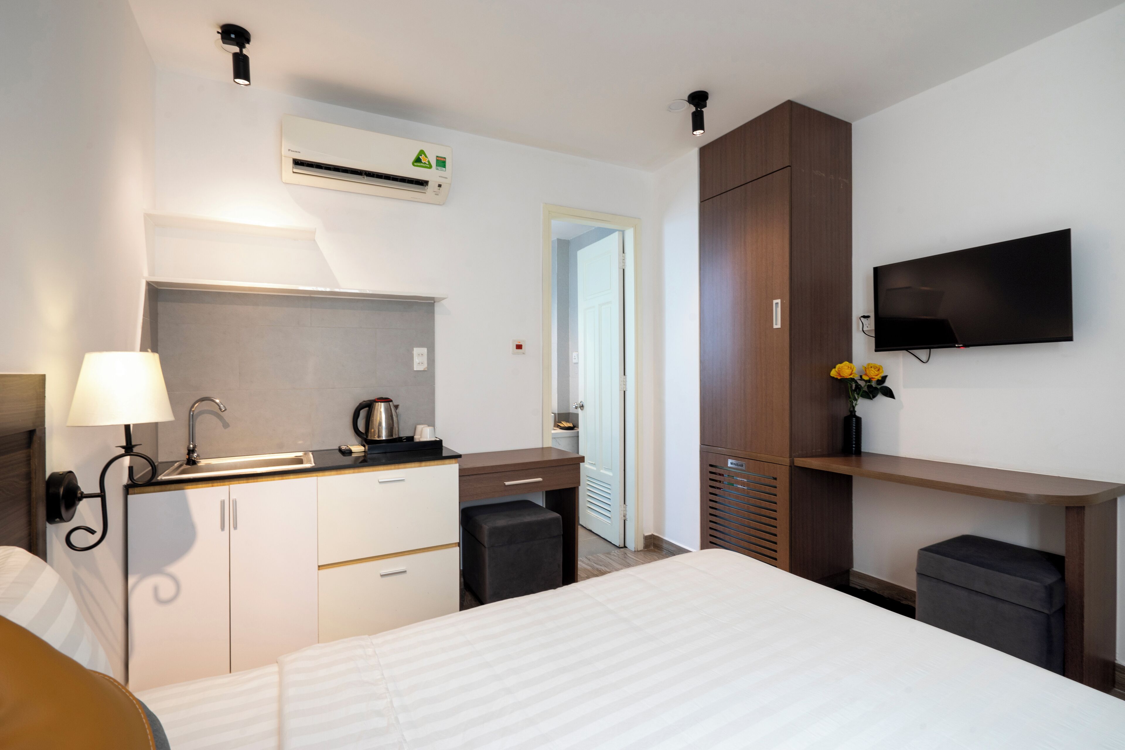 A hotel room with a bed, a desk with a sink, a flat-screen TV, and a wardrobe.
