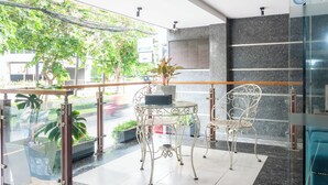 Un espacio interior con paredes de vidrio, muebles de metal, una planta en maceta y vistas a la calle.