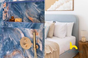 A bathroom with a marble wall, a gold showerhead, and a soap dish. The room has a bed with white bedding and a nightstand with a lamp. - Aegean Blue Hideaway w/ Fireplace, near Acropolis (Athens)
