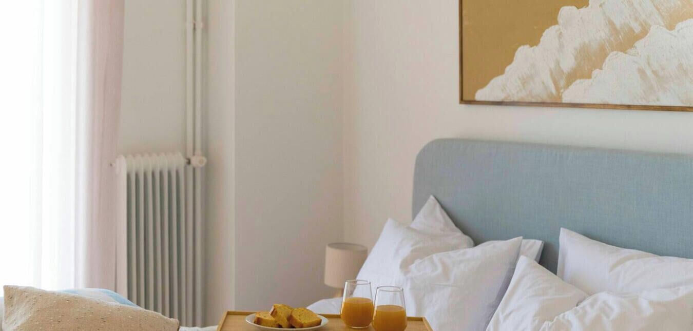 Ein Hotelzimmer mit einem Bett, Kissen, einem Nachttisch mit Toast und zwei Gläsern Orangensaft sowie einer Heizung.