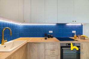 A modern kitchen with blue tiles, a gold faucet, wooden cabinets, and a dishwasher. - Aegean Blue Hideaway w/ Fireplace, near Acropolis (Athens)