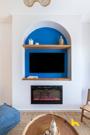 A living room with a blue arched shelf above a fireplace, a flat-screen TV, and a round wooden table with a vase. - Aegean Blue Hideaway w/ Fireplace, near Acropolis (Athens)