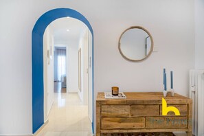 A hallway with a blue archway leading to a bedroom. A wooden dresser with a mirror and candles is against the wall. - Aegean Blue Hideaway w/ Fireplace, near Acropolis (Athens)