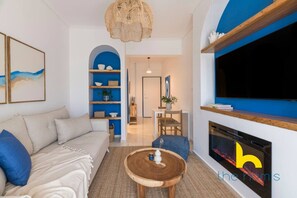 A modern living room with a sofa, coffee table, and TV. There is a fireplace and a dining area in the background. - Aegean Blue Hideaway w/ Fireplace, near Acropolis (Athens)