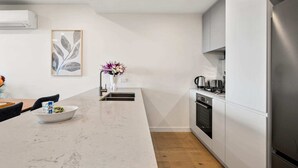 Una cocina moderna con encimera de mármol, electrodomésticos de acero inoxidable y una mesa de comedor de madera con sillas.