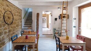A dining area with wooden tables and chairs, a staircase, and a kitchen visible in the background. - The Oak and the Donkey. (Piazza Armerina)