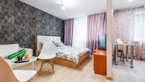 A modern hotel room with a large bed, a desk with a TV, a small table with chairs, and a couch.