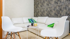 A modern living room with a white sectional sofa, two white chairs, a small round table, and a decorative wall with a geometric pattern.