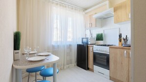 A compact kitchen with a dining area, featuring a refrigerator, stove, and a small countertop with a microwave.