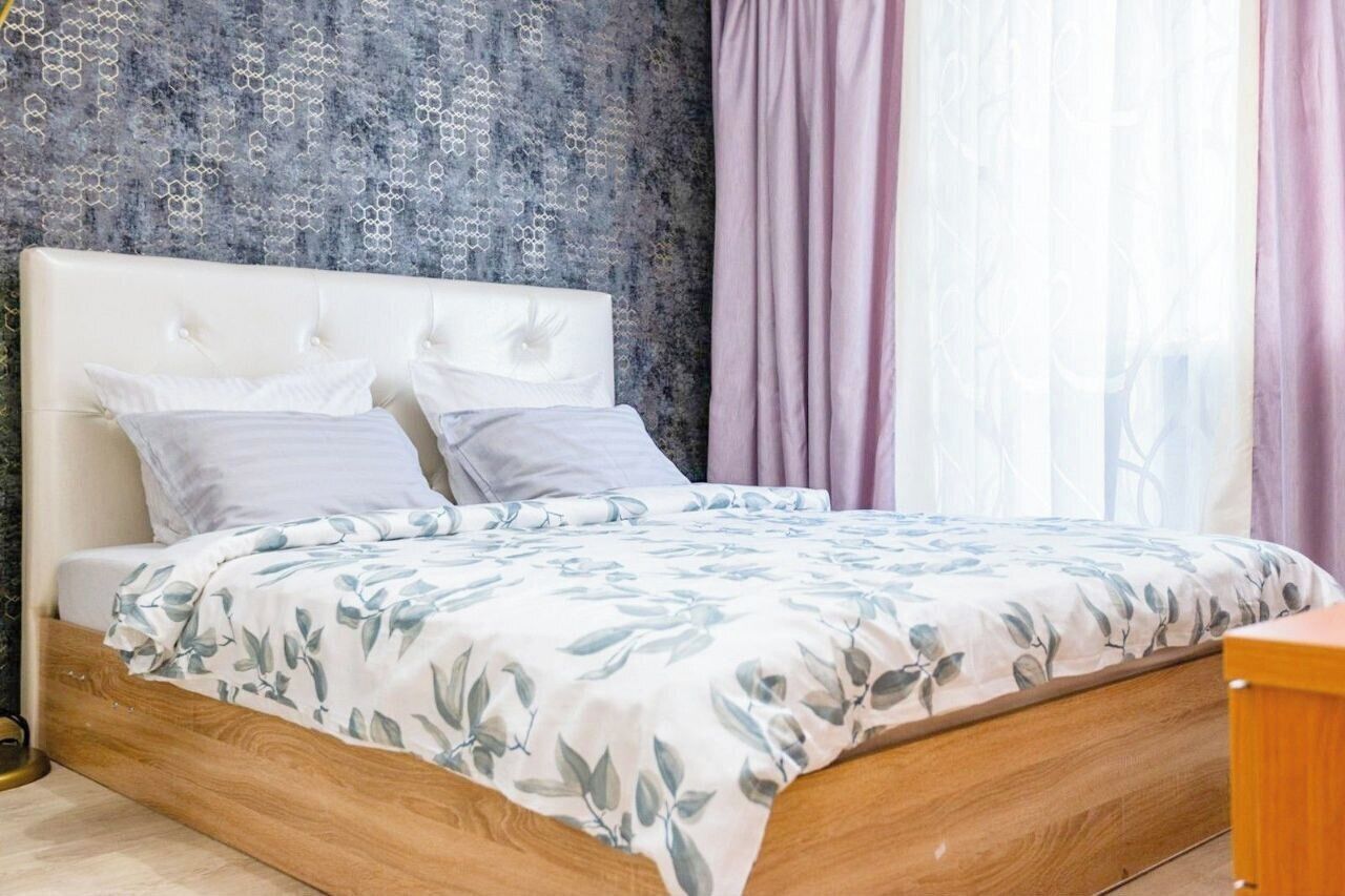 Ein Schlafzimmer mit einem Bettgestell aus Holz, einem weißen gepolsterten Kopfteil und einer blumigen Tagesdecke.