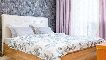 Ein Schlafzimmer mit einem Bettgestell aus Holz, einem weißen gepolsterten Kopfteil und einer blumigen Tagesdecke.