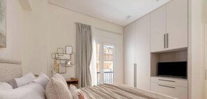 Ein Schlafzimmer mit einem Bett, einem Fernseher, Schränken und einem Fenster mit Vorhängen.