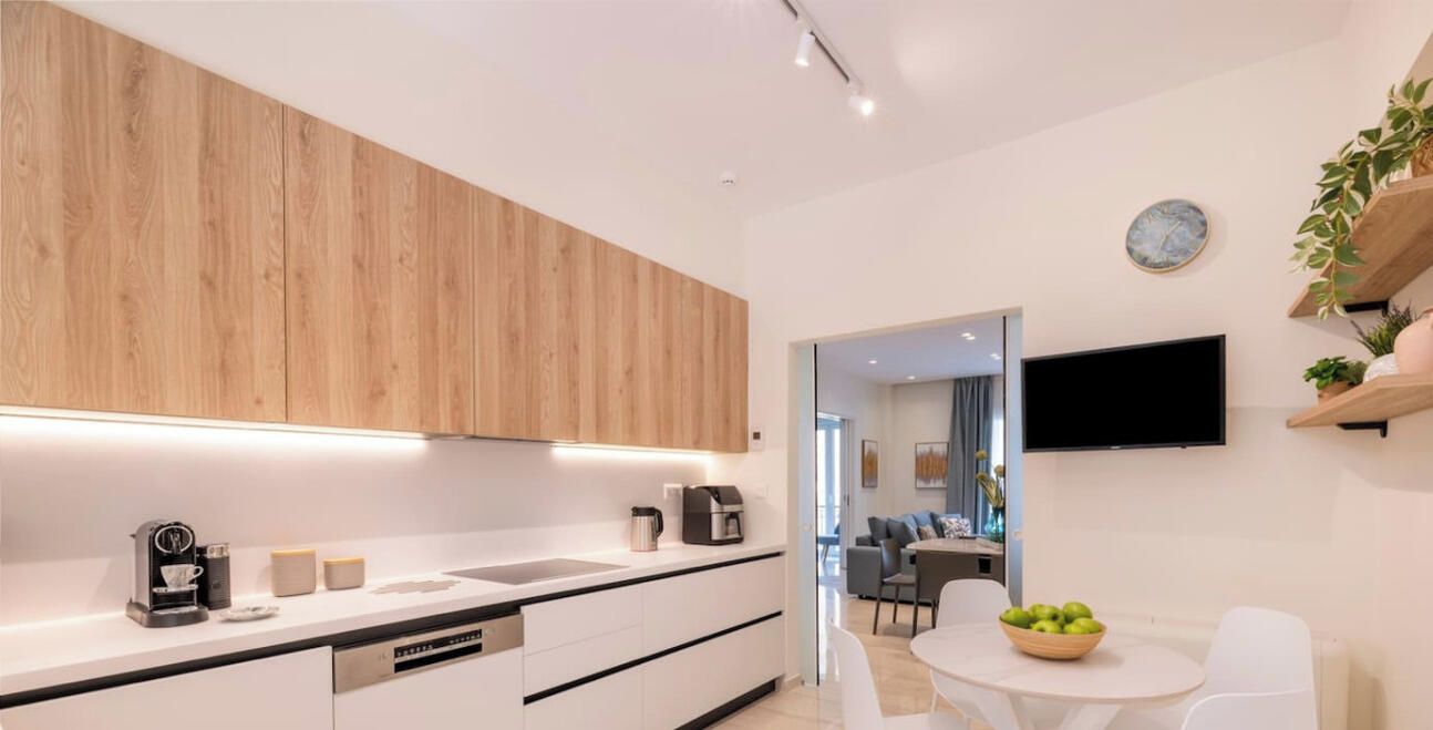 A modern kitchen with wooden cabinets, a built-in dishwasher, and a dining area with a white table and chairs.