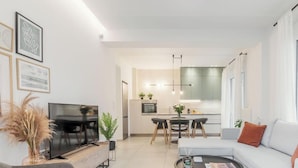 Uma sala de estar moderna com televisão de tela plana, um sofá e um espaço de refeições com mesa e cadeiras.