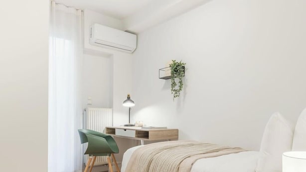 Quarto com cama, escrivaninha, cadeira, radiador, ar condicionado e uma planta fixada na parede.