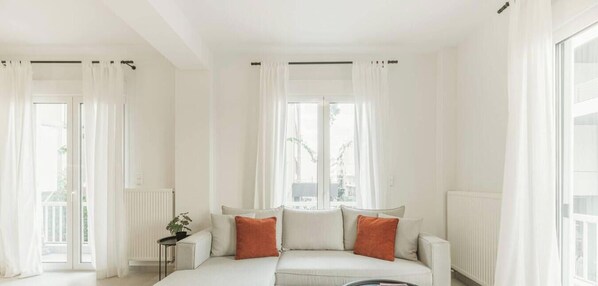 A modern living room with a sofa, a small side table, and a view through large windows. - Stylish 2 bdr apt in centre of Athens by The Homis (Athina)